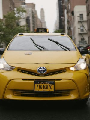 Front view of a yellow taxi cab driving through a bustling New York City street.