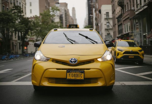 Front view of a yellow taxi cab driving through a bustling New York City street.